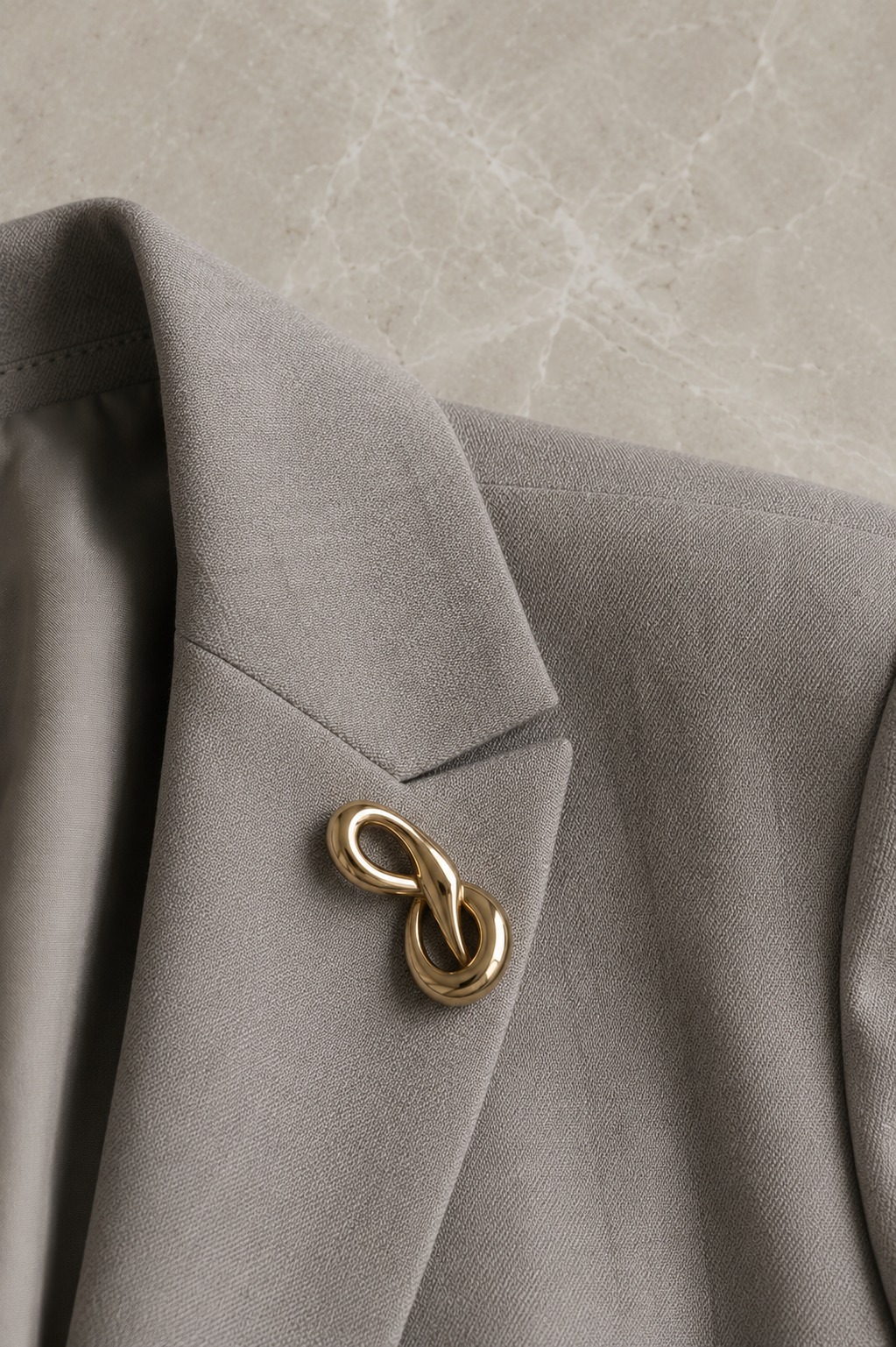 Close-up de broche dourado sobre lapela de blazer cinza — sofisticação no detalhe