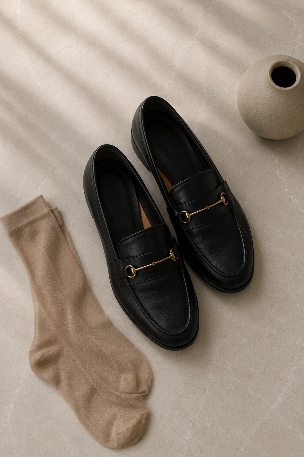 Flat lay de loafer de couro com detalhe de metal dourado — o calçado que define o look elegante