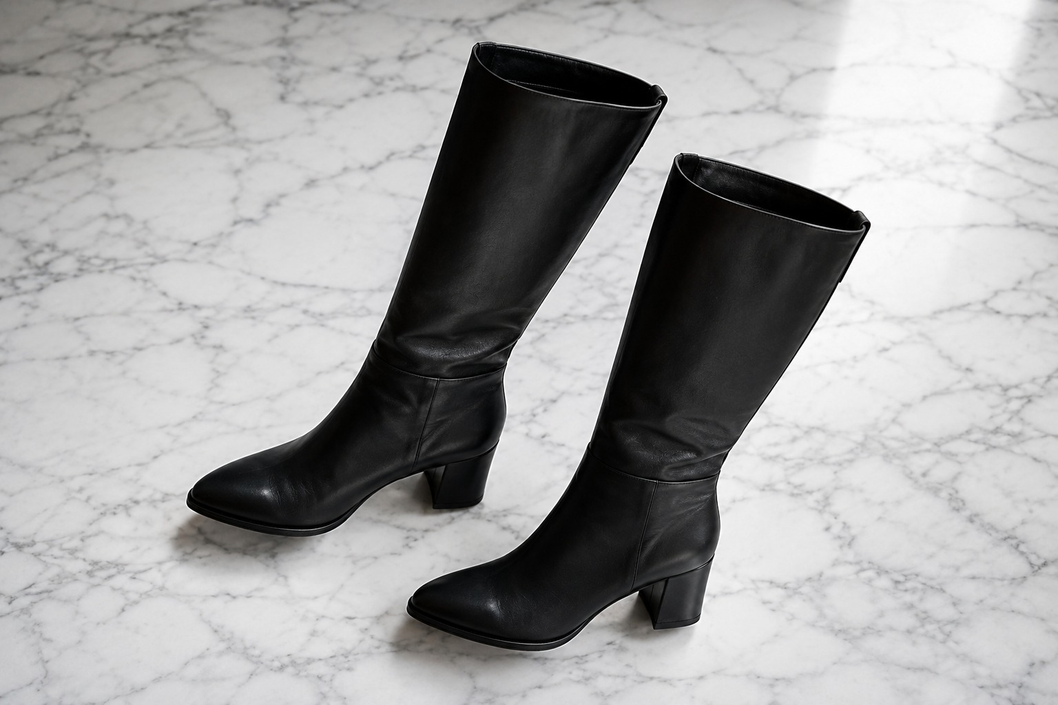 Flat lay de bota cano longo feminina em couro preto sobre superfície de mármore — look de inverno