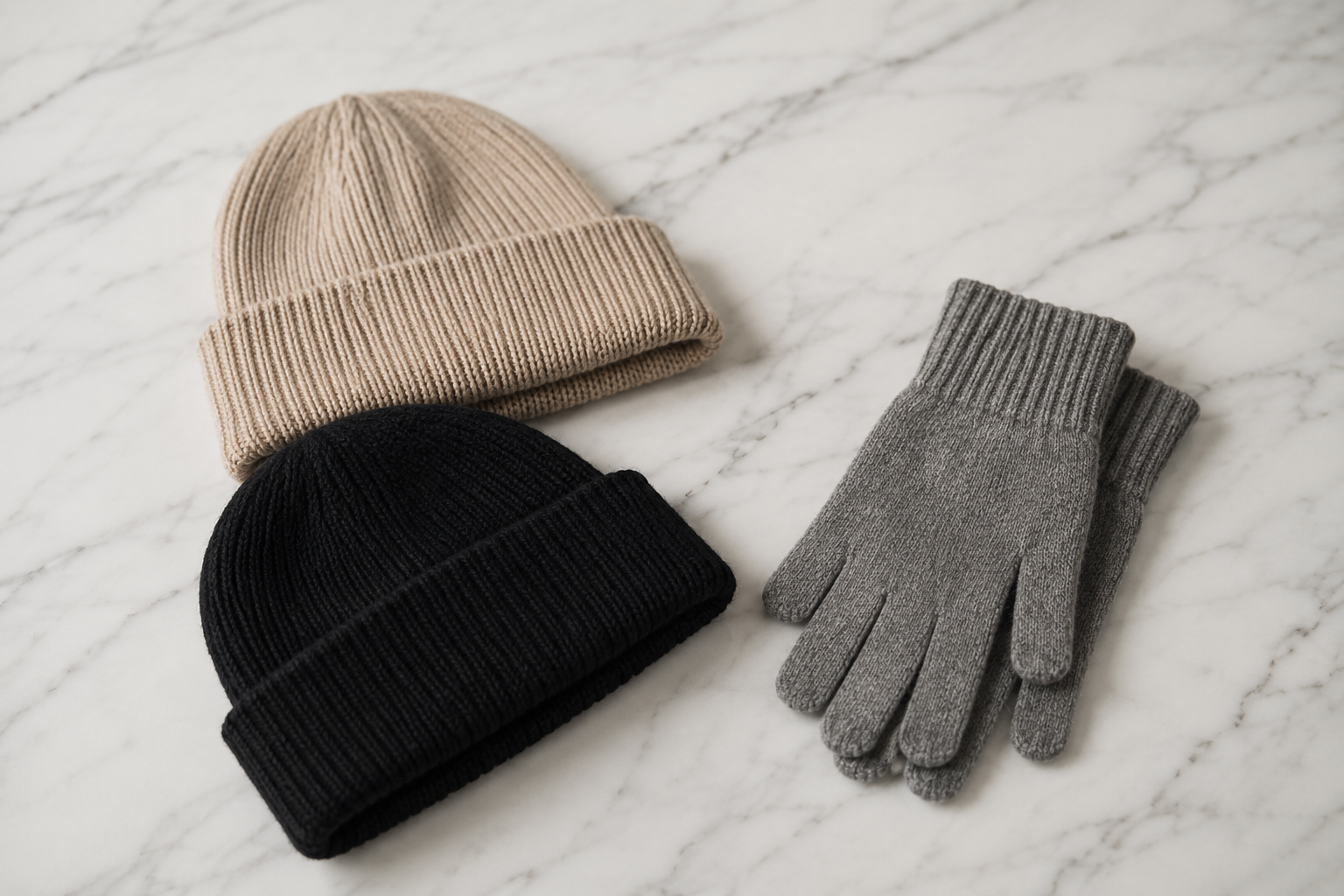 Dois gorros de tricô bege e preto ao lado de luvas de lã cinza